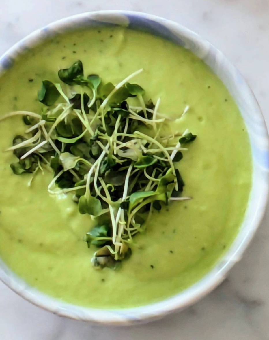 A bowl of chilled green avocado cucumber soup topped with broccoli sprouts